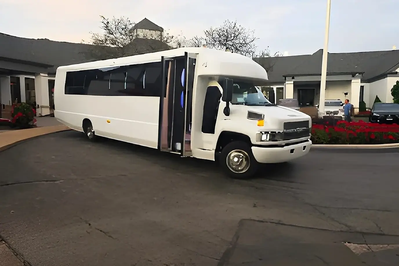 White party bus at a hotel entrance lined with red flowers