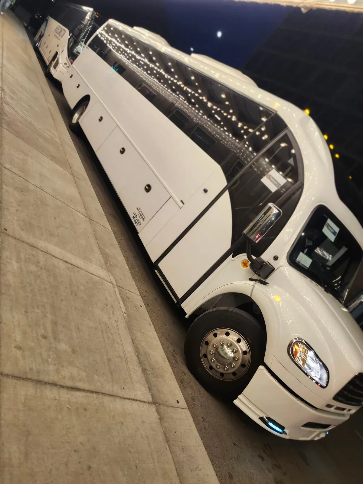 White limo coach with string-lit windows parked at a downtown curb at night