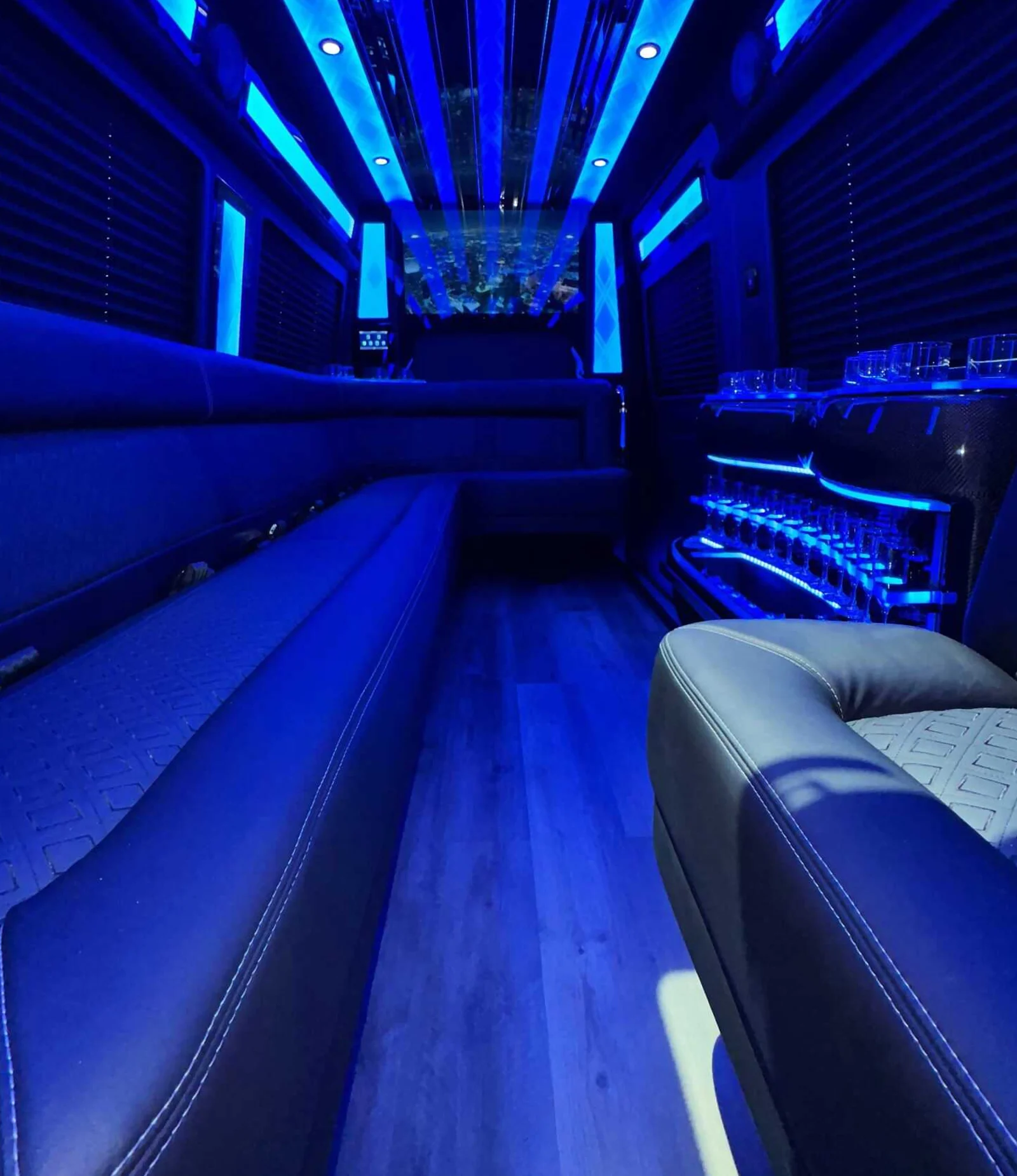 Sprinter Limo interior with blue LED lighting, facing bench seating, and a lit glassware bar